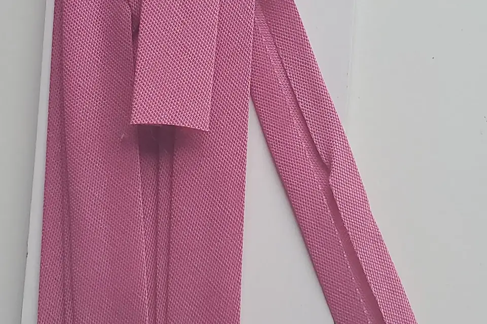 Bandes de biais simple rose posées sur un fond blanc, dont on voit les deux bords repliés vers le centre