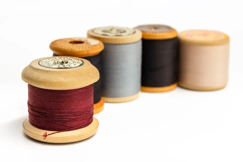 Cinq bobines de fil anciennes en bois, bordeaux au premier plan, puis noir, gris, noir et beige