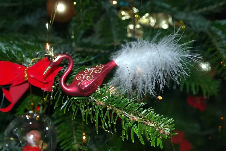 Décoration de Noël en forme de cygne rouge et or, à queue de plumes blanches, suspendue dans un sapin près d'un nœud rouge
