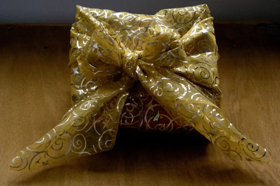 Cadeau enveloppé dans un carré de tissu noué sur le dessus, posé près d'un sapin de Noël