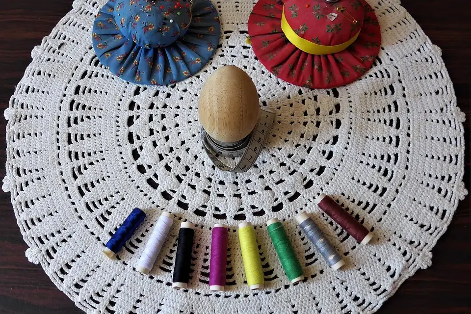 Sur un napperon au crochet, deux pelotes à épingles en tissu, un œuf à repriser entouré d'un mètre ruban et une rangée de bobines de fil de couleur