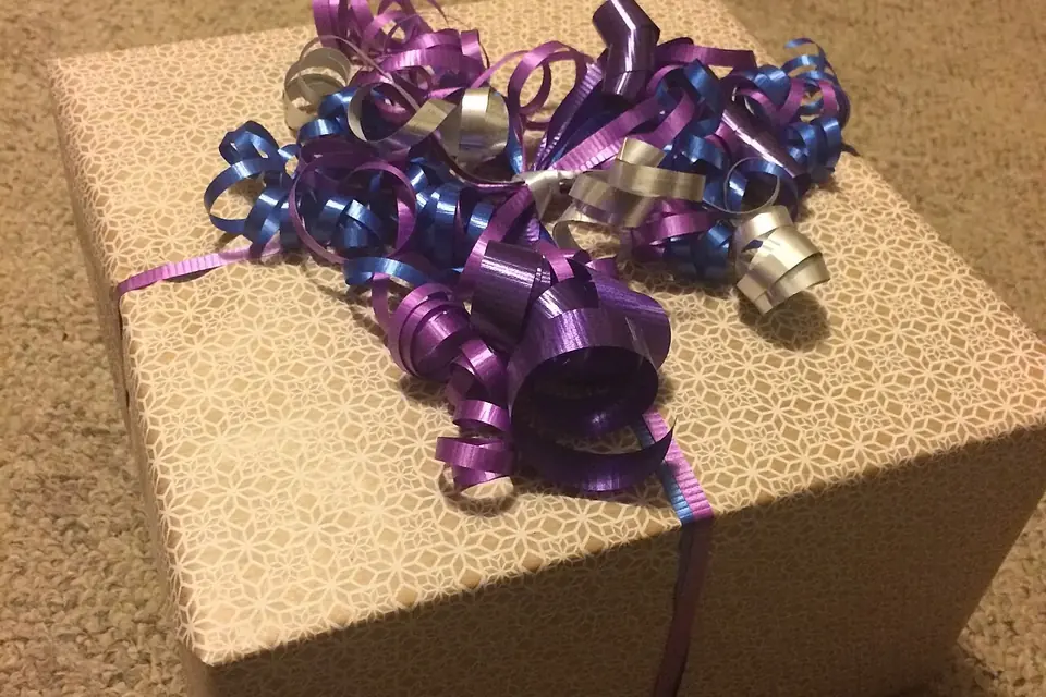 Paquet cadeau emballé de papier clair, entouré d'un ruban violet et coiffé de boucles de ruban frisé violet, bleu et argent