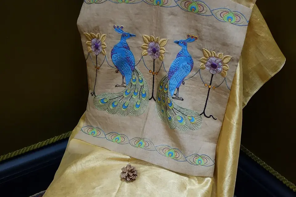 Panneau de lin brodé et peint de deux paons bleus se faisant face, entre des fleurs stylisées, avec une frise d'ocelles de plumes de paon