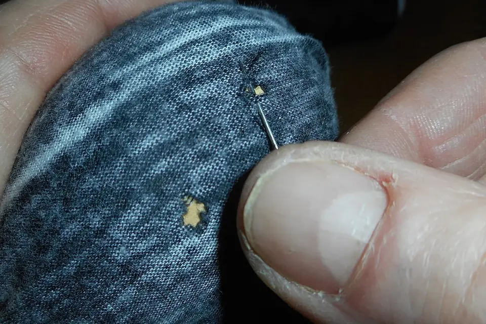 Mains tenant un tricot gris tendu sur un champignon à repriser, une aiguille piquée au bord d'un petit trou