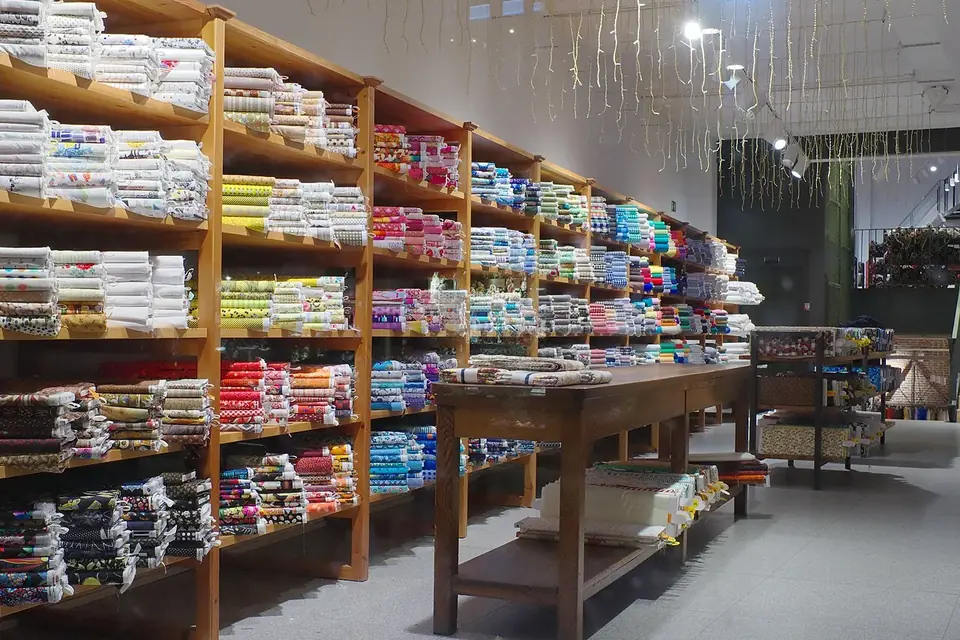 Grande salle aux étagères de bois chargées de rouleaux de tissus colorés, avec une longue table de coupe au centre