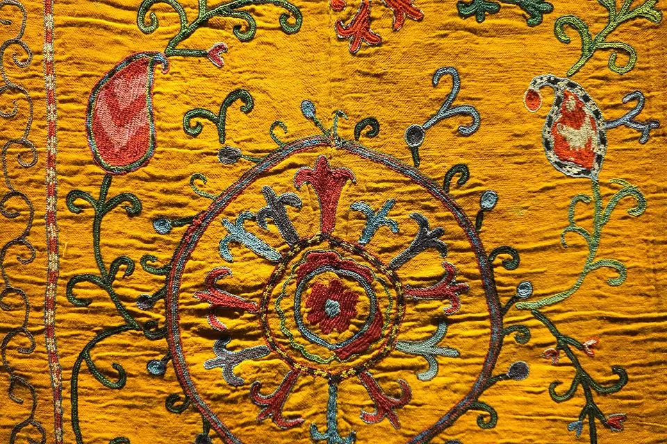 Broderie ancienne sur fond jaune safran : un grand disque rayonnant brodé en rouge, brun et vert, entouré de rinceaux et de fleurs